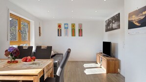 Un salon moderne comprenant une table à manger, des chaises, un canapé, un téléviseur et des œuvres d’art accrochées aux murs.