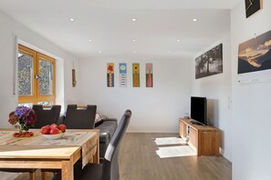 Un soggiorno moderno con un tavolo da pranzo, sedie, un divano, una TV e opere d'arte alle pareti.