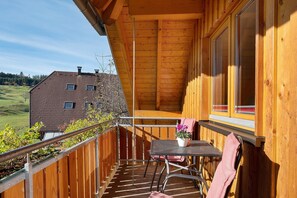 A wooden balcony with a table and chairs, a potted plant, and a view of a house. - Apartment 'Talblick, 75sqm' with Mountain View, Balcony and Wi-Fi (Elzach)