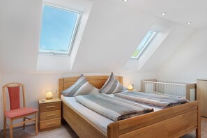 A bedroom with a sloped ceiling, skylights, a wooden bed, a bedside table, a chair, and a crib. - Apartment 'Talblick, 75sqm' with Mountain View, Balcony and Wi-Fi (Elzach)