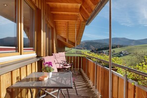 A wooden balcony with a table and chairs, a potted plant, and a view of a green landscape with hills. - Apartment 'Talblick, 75sqm' with Mountain View, Balcony and Wi-Fi (Elzach)