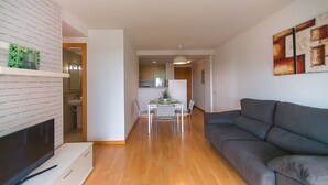 A modern living room with a grey sofa, a flat-screen TV, and a dining area with a table and chairs. - WELCS APARTMENT 287 EMP with public swimming pool (Rosas / Roses)