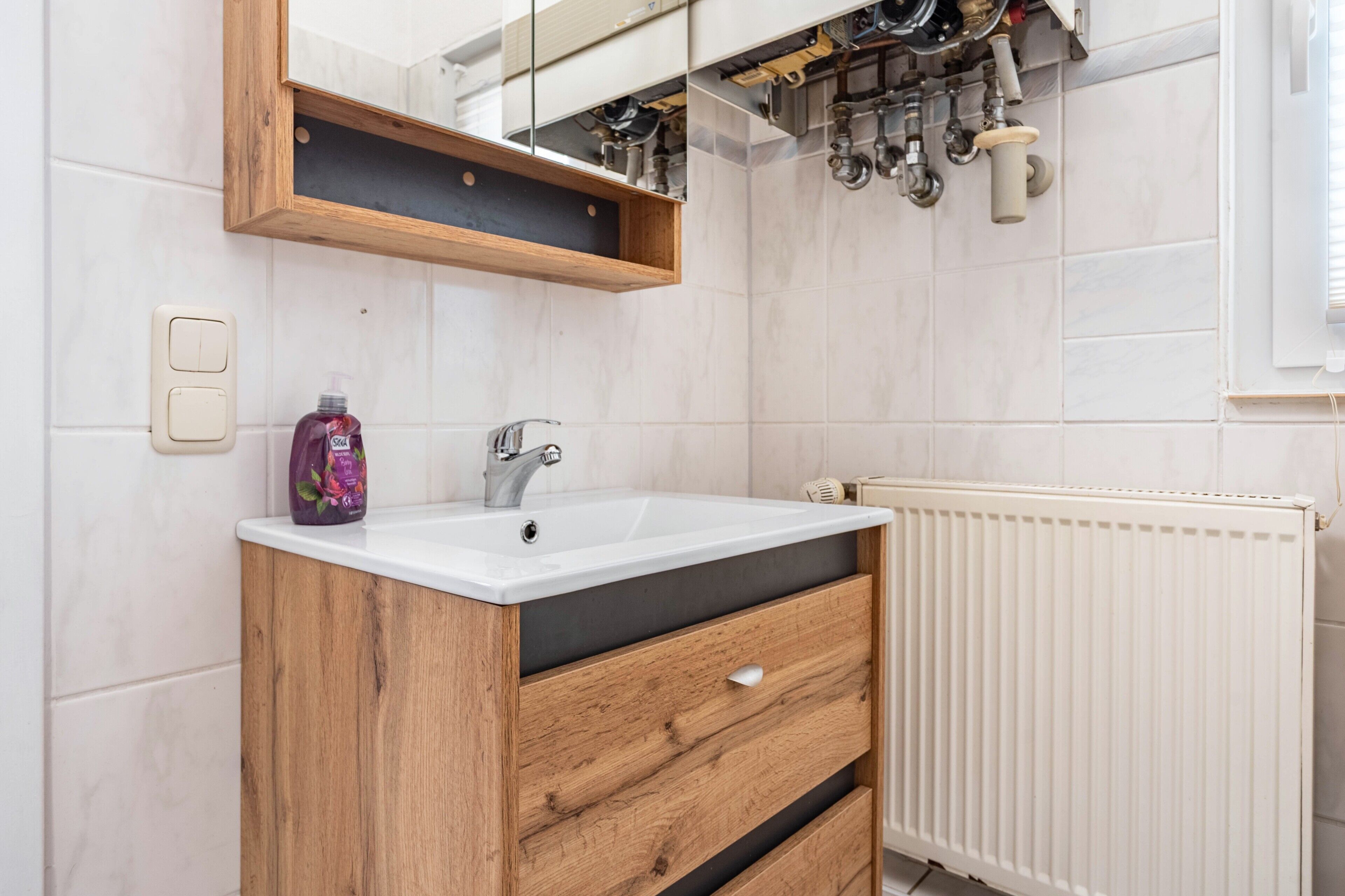 Een badkamer met een houten wastafelmeubel, een witte wasbak, een spiegel en een radiator.