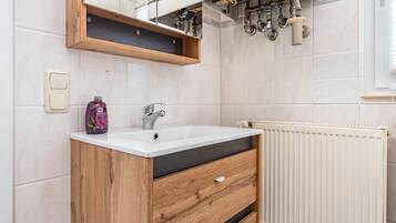 Een badkamer met een houten wastafelmeubel, een witte wasbak, een spiegel en een radiator.