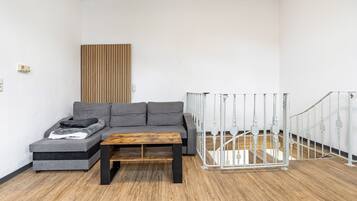 A modern living room with a grey sofa, a wooden coffee table, and a white railing.