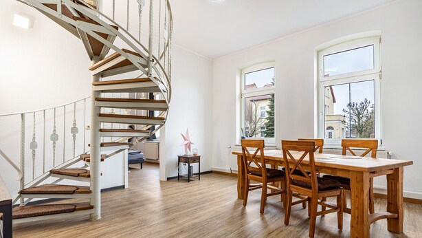 A spiral staircase, a dining table with chairs, and a window with a view of a building.