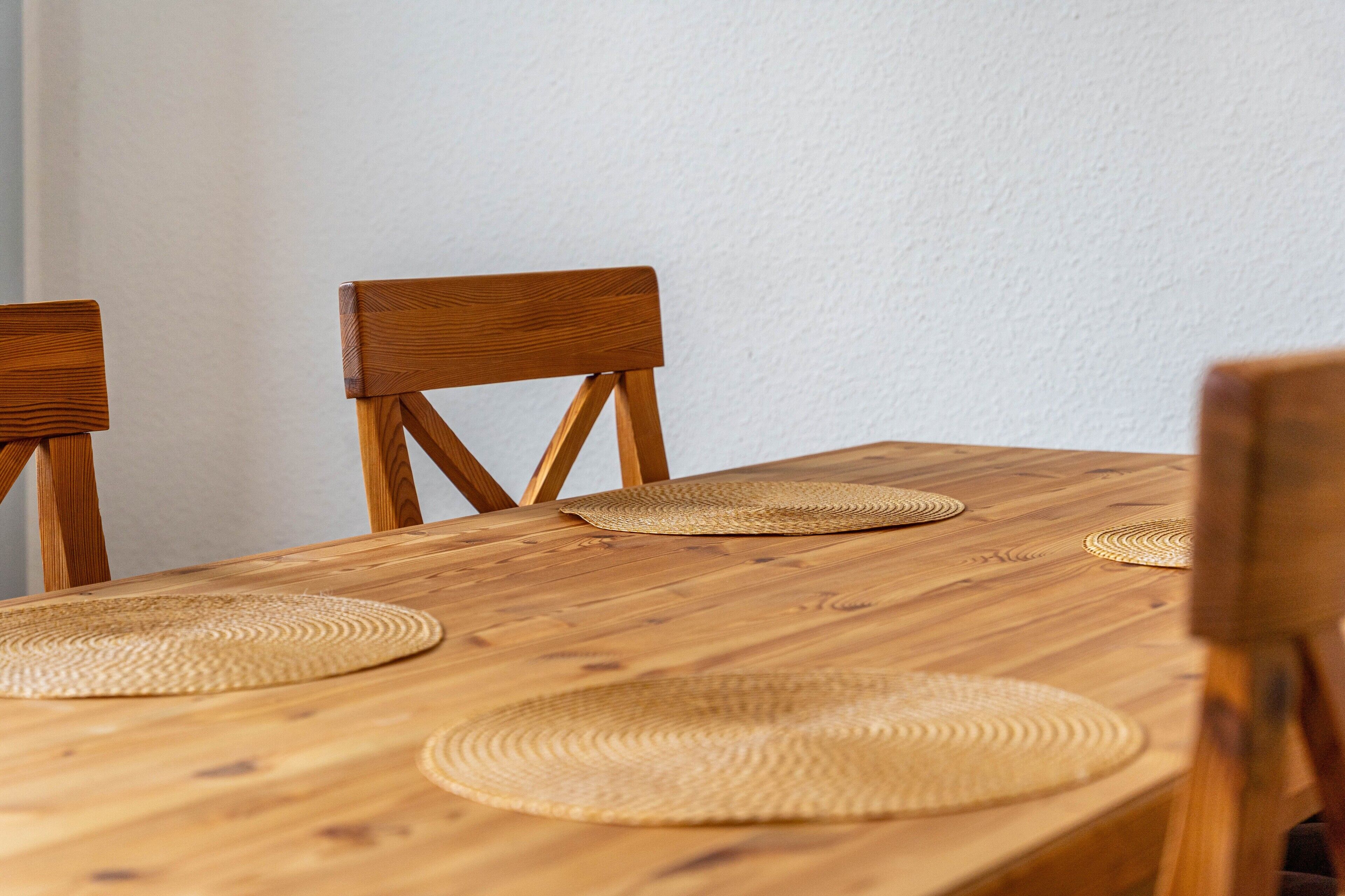 A wooden dining table with woven placemats and matching chairs.