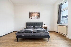 A bedroom with a bed, a nightstand, a lamp, a window, and a painting on the wall.