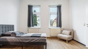 A bedroom with a bed, a chair, two windows, and a radiator.