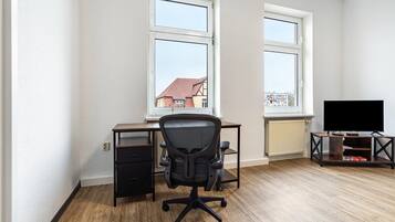 Ein Zimmer mit Schreibtisch, Bürostuhl, Fernseher und Fenstern.