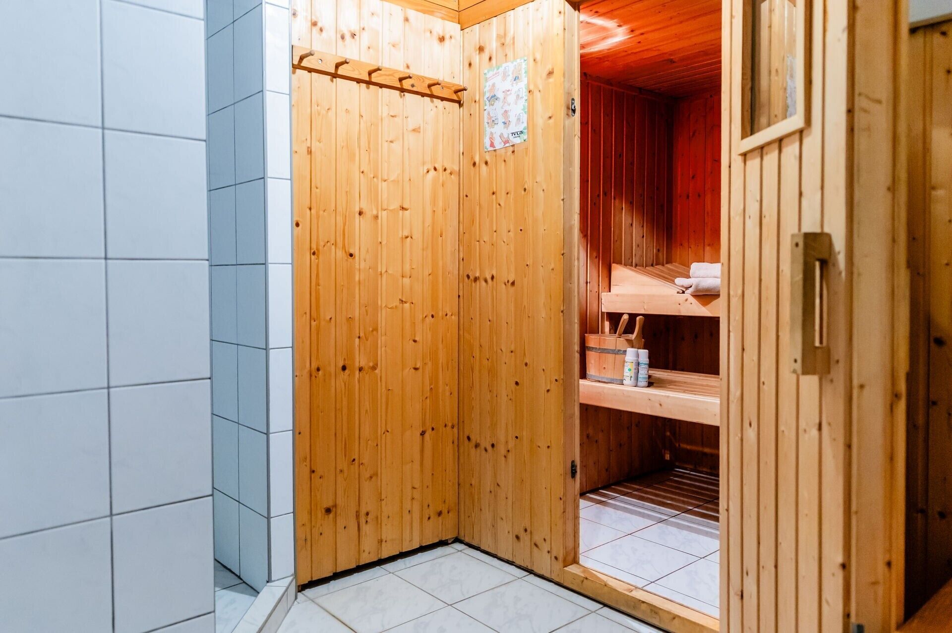 A sauna room with wooden walls, a tiled floor, and shelves with towels and bottles.