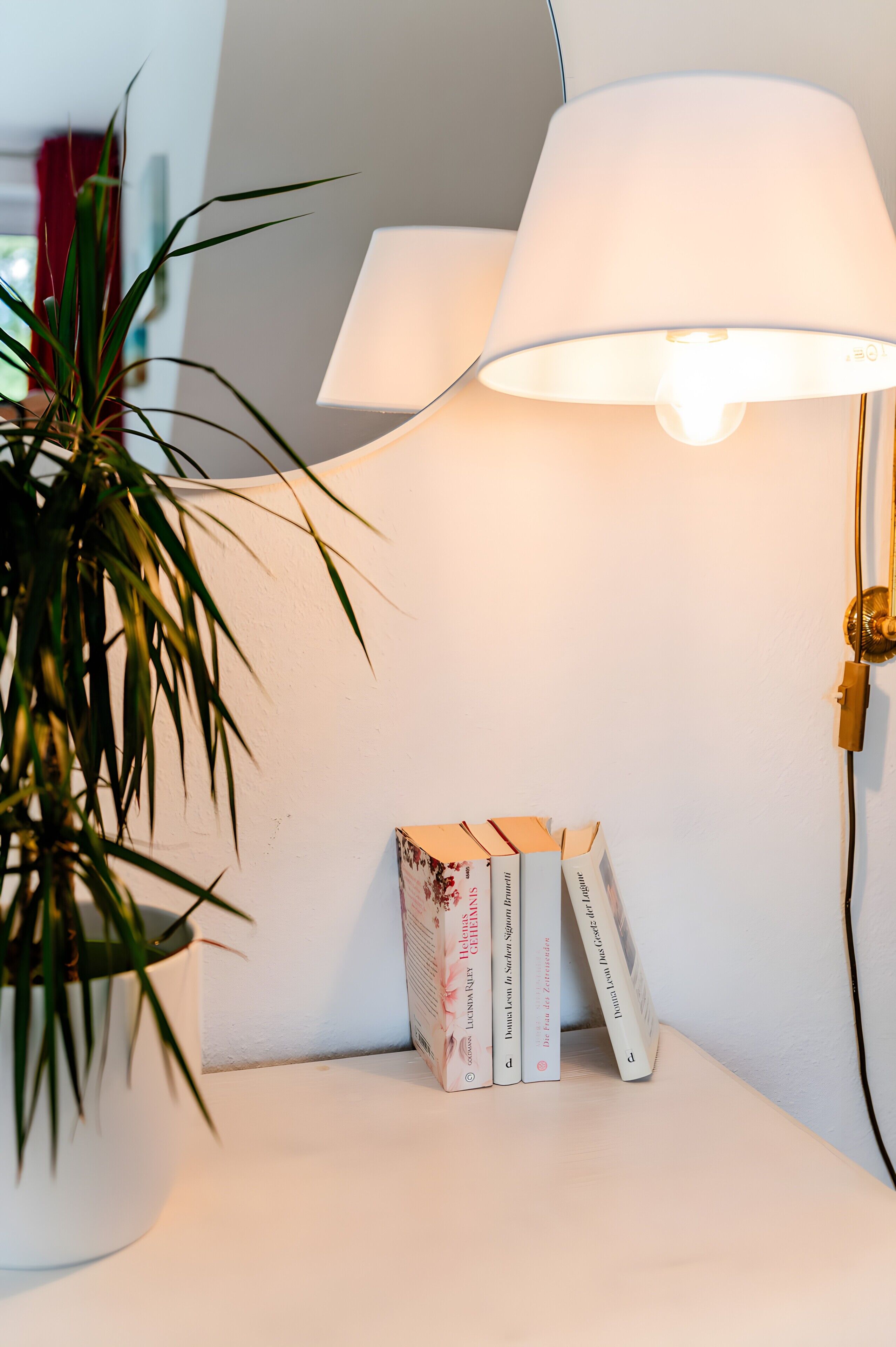 Et hvidt bord med en lampe, en potteplante og en stak bøger.
