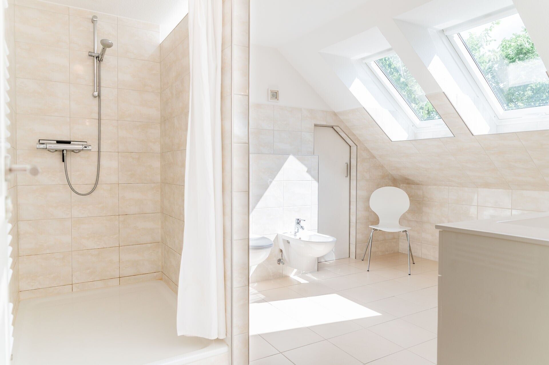 Ein modernes Badezimmer mit Dusche, Toilette und Waschbecken, ausgestattet mit Dachfenstern und einer geneigten Decke.