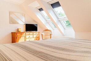A bedroom with a bed, a dresser, a television, a wicker chair, and skylights. - Holiday Home 'Seeblick' with Sea View, Private Terrace and Wi-Fi (Langballig)