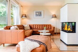 A modern living room with a leather sofa, a fireplace, and two floor lamps. - Holiday Home 'Seeblick' with Sea View, Private Terrace and Wi-Fi (Langballig)