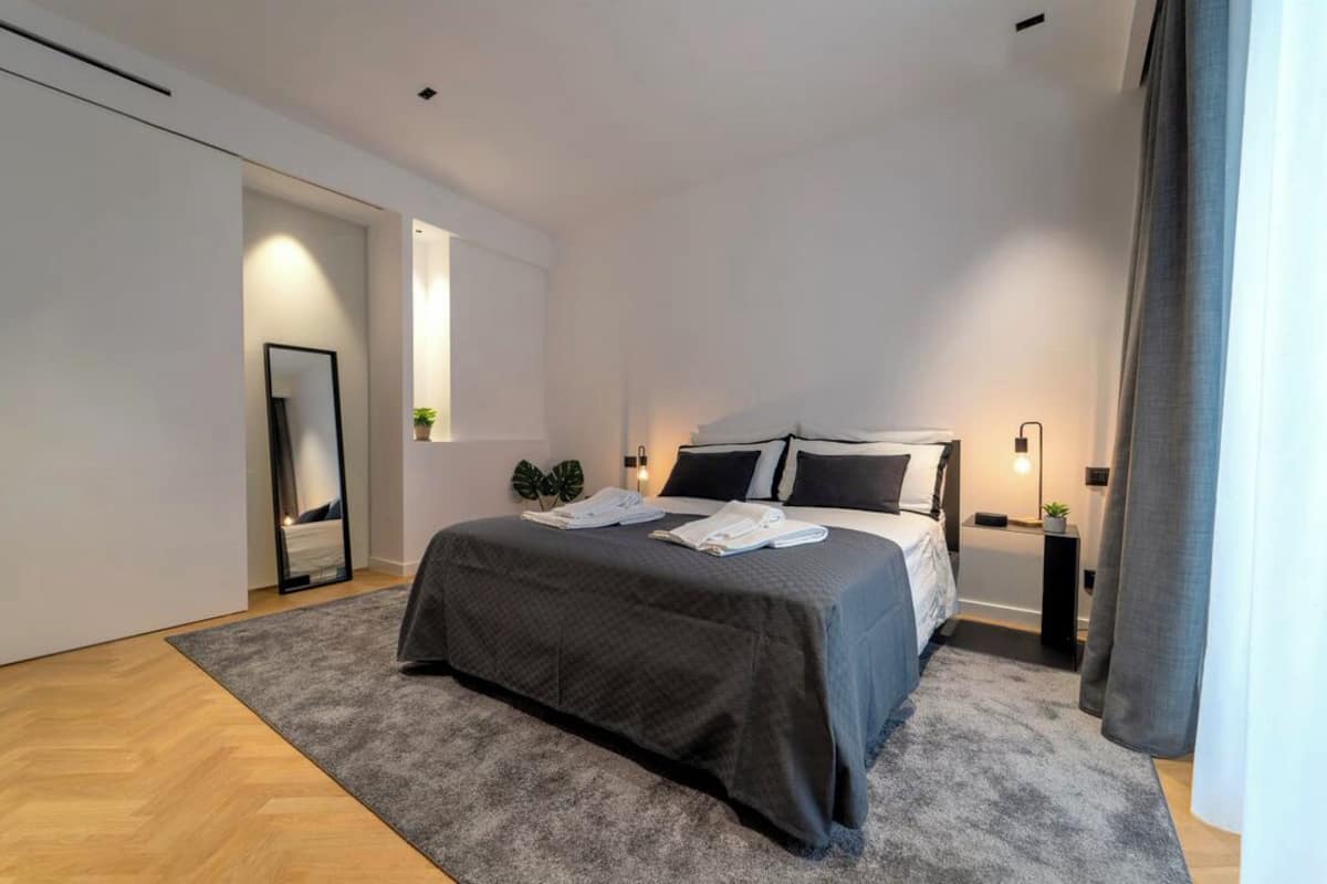 A modern bedroom with a large bed, a bedside table, a mirror, and a small plant.