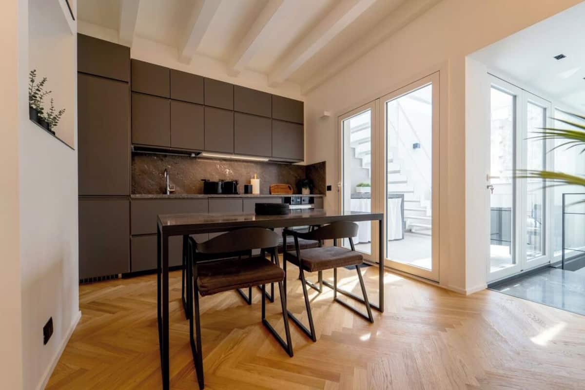 A modern kitchen with dark cabinets, a wooden dining table, and chairs.