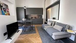 A modern living room with a grey sofa, a flat-screen TV, and a dining area with a table and chairs. - Gonia Residence (Trapani)