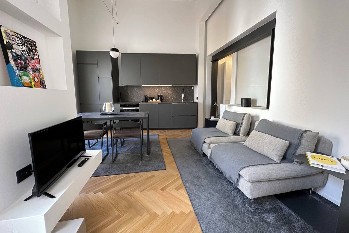 A modern living room with a grey sofa, a flat-screen TV, and a dining area with a table and chairs.