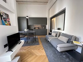Una sala de estar moderna con un sofá gris, un televisor de pantalla plana y una zona de comedor con mesa y sillas.