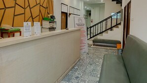A reception area with a counter, a wall-mounted clock, a staircase, and a sign for 'TAMASTU Peraturan Tata Tertib Passer Baroe Inn'. - PBINN Tamastu House Pasar Baru (Jakarta)