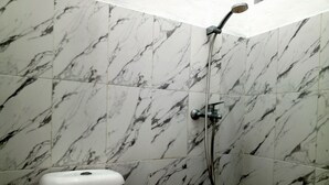 A bathroom with marble tiles, a toilet, and a shower with a handheld showerhead. - PBINN Tamastu House Pasar Baru (Jakarta)