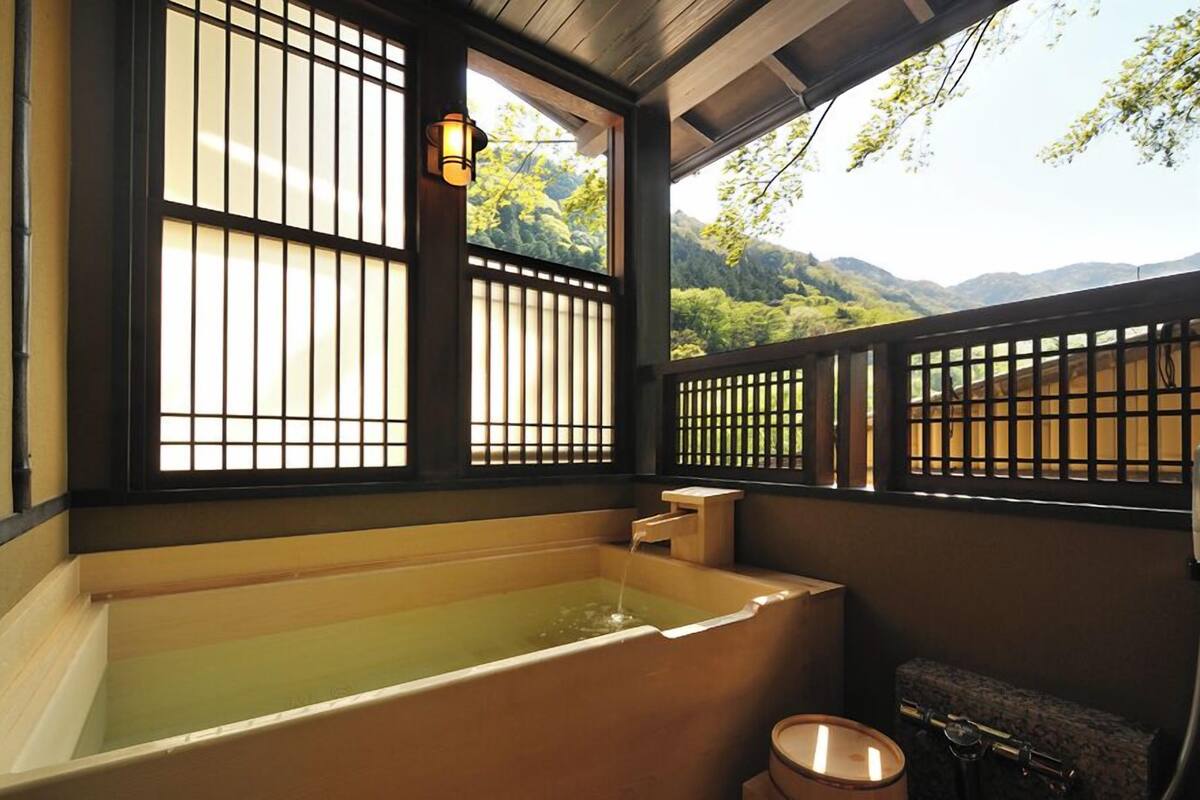 Un onsen japonés tradicional con una bañera de madera, puertas correderas y vistas a la montaña.