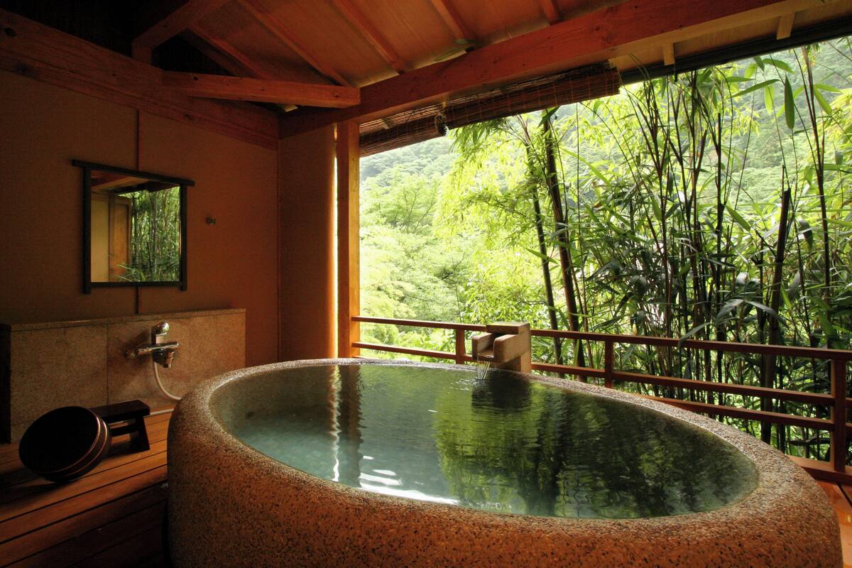 Un área de spa con un jacuzzi, vigas de madera, un espejo y vistas a un bosque de bambú.