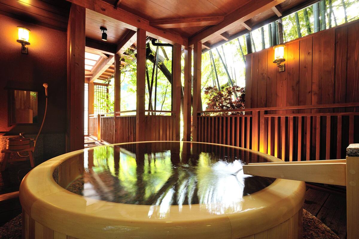 Un onsen japonés tradicional con arquitectura de madera, un baño de aguas termales y luz natural gracias a amplias ventanas.
