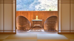 Une pièce de style japonais traditionnel, avec un sol recouvert de tatamis, deux chaises en osier et une petite table ornée de bougies.