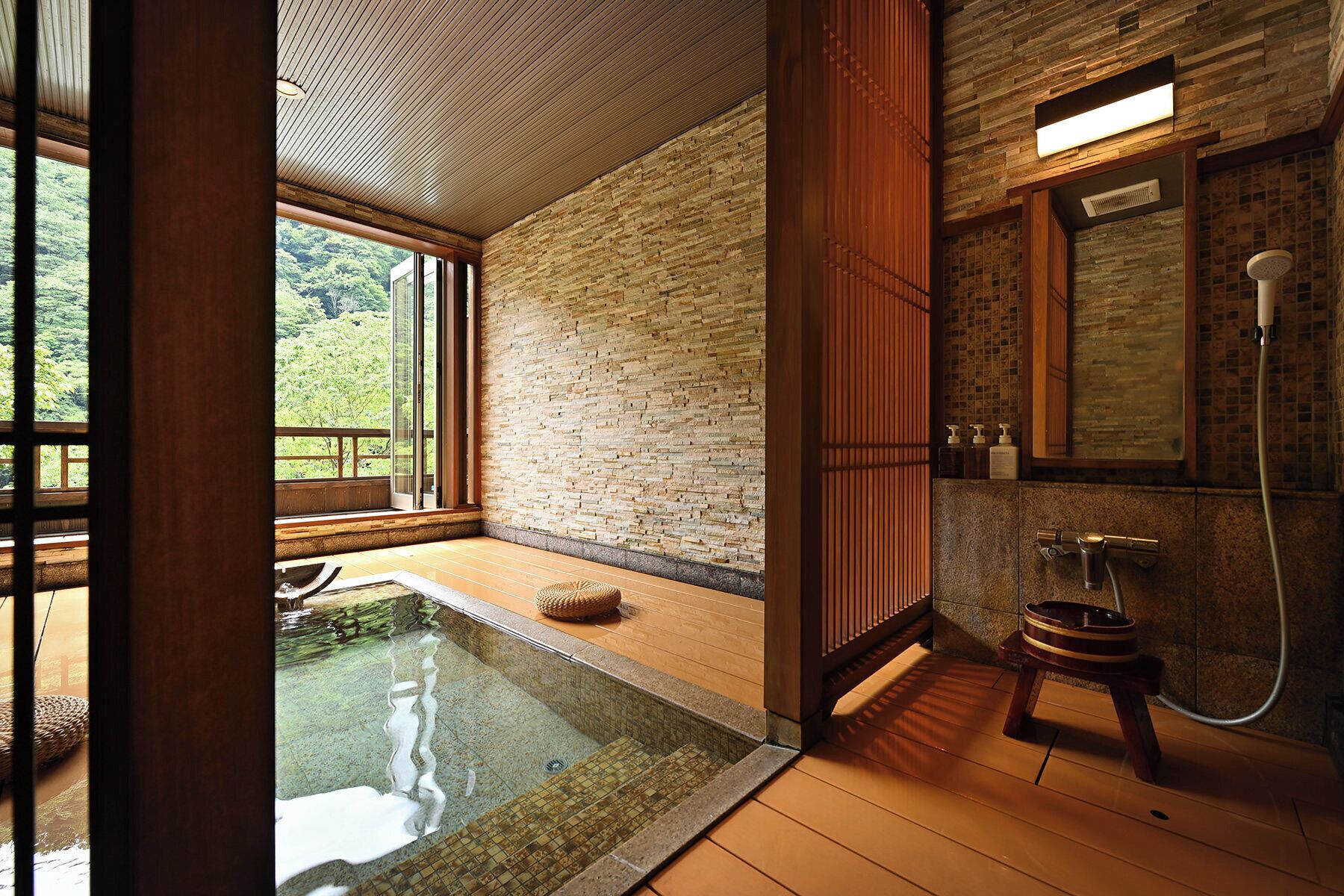 A modern bathroom with a stone wall, a wooden floor, and a glass-enclosed hot tub.