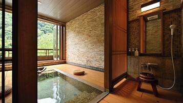 A modern bathroom with a stone wall, a wooden floor, and a glass-enclosed hot tub.