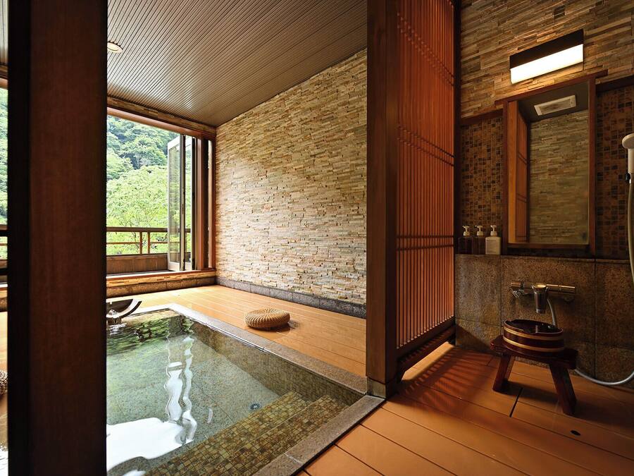 A modern bathroom with a stone wall, a wooden floor, and a glass-enclosed hot tub.