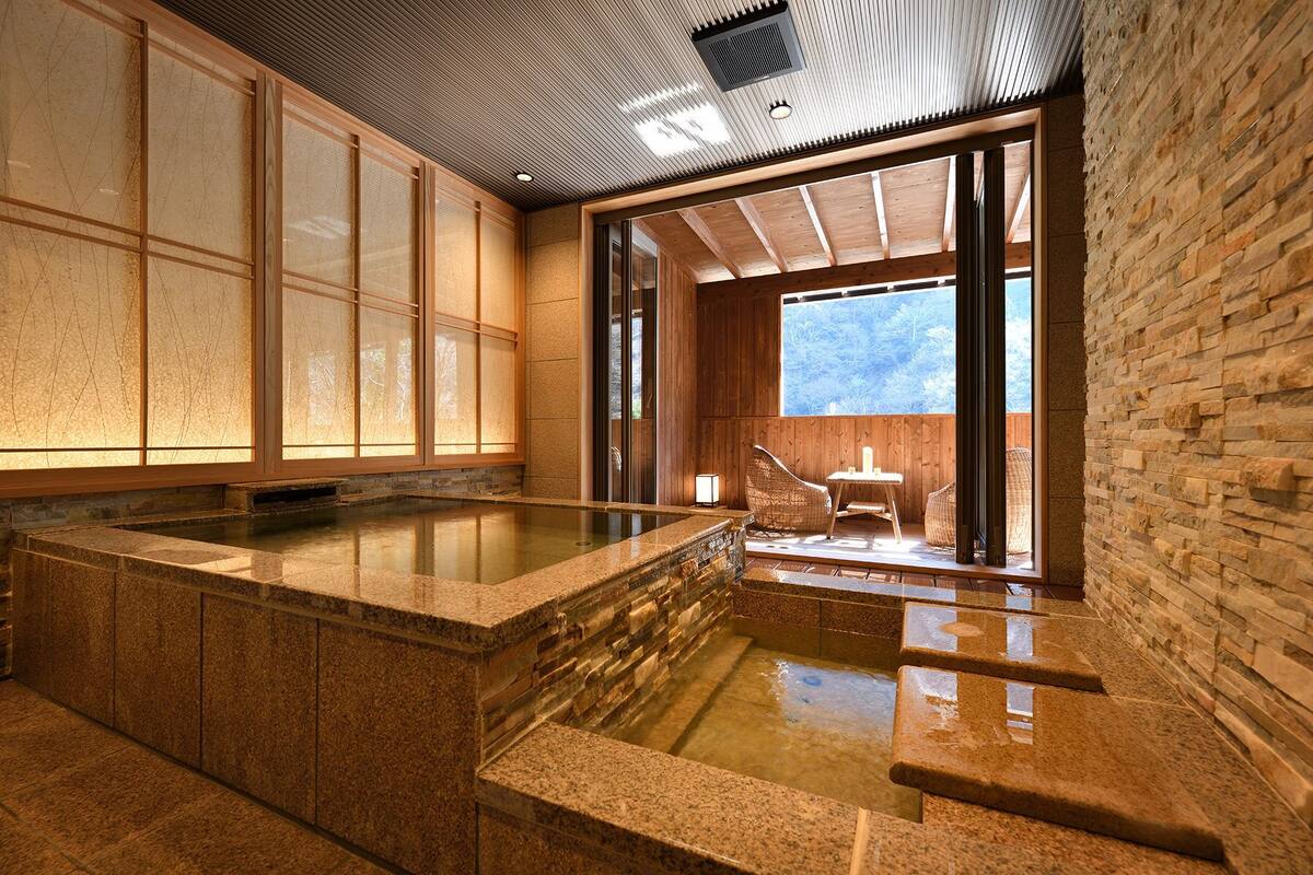 Un onsen japonés tradicional con un manantial de piedra caliente, puertas correderas de madera y vistas al exterior.
