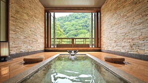 A spa area with a large rectangular pool, wooden flooring, and a view of a forest through large windows.