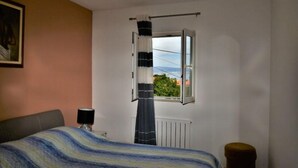 Ein Schlafzimmer mit Bett, einem Fenster mit Vorhängen, einem Heizkörper und einem Gemälde an der Wand.