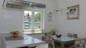 Eine moderne Küche mit Einbauherd, einem Esstisch mit floralen Stühlen und einem Fenster mit Blick ins Grüne.