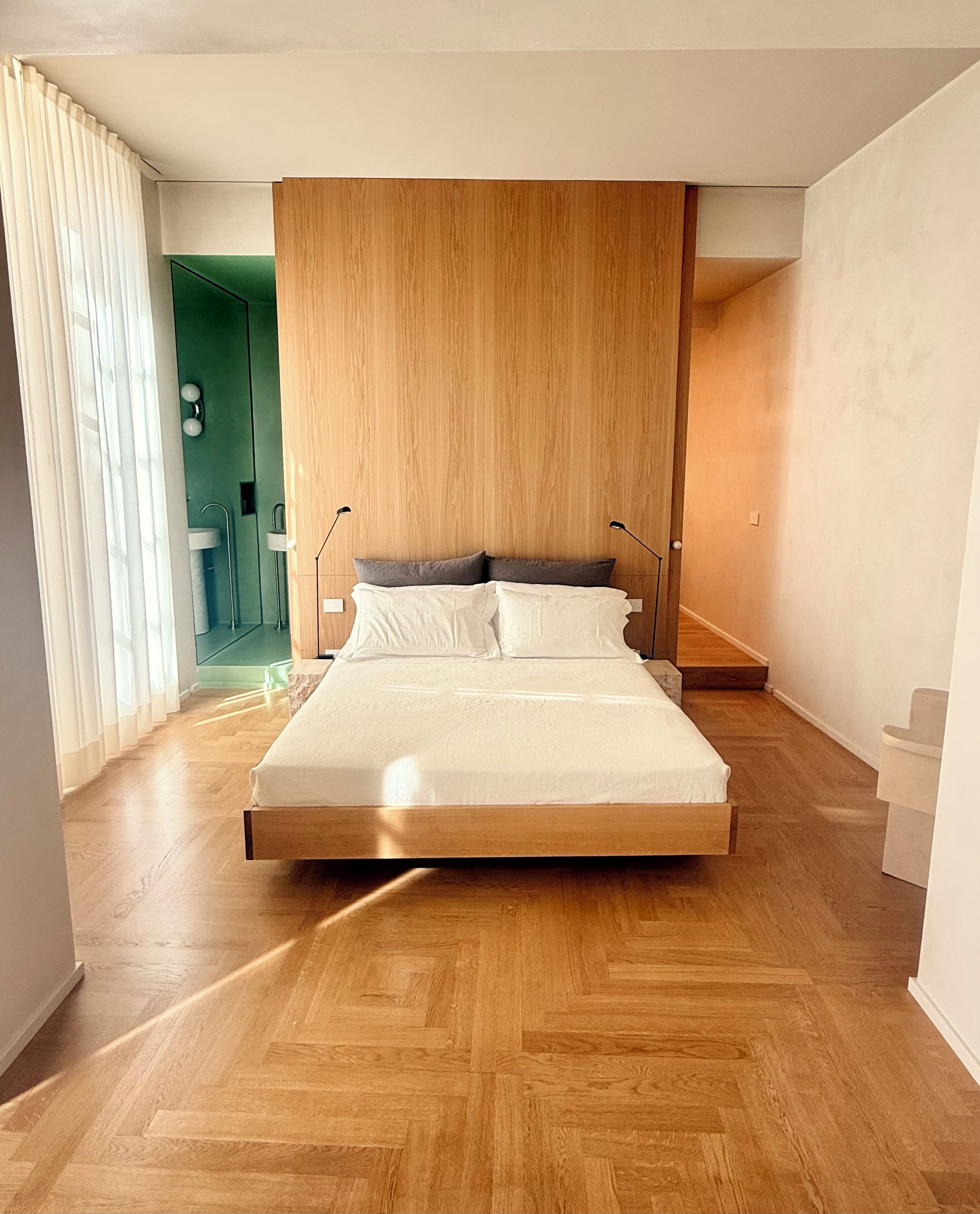 Une chambre à coucher moderne avec un plancher en bois, un grand lit avec une literie blanche et un mur d’accent vert.
