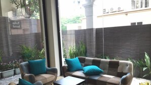 Una sala de estar moderna con un sofá y sillones, una mesa de centro, y un ventanal con vistas a un jardín y un edificio.