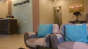 Zona de recepción de un hotel con mostrador, un sofá con cojines azules y una escalera.