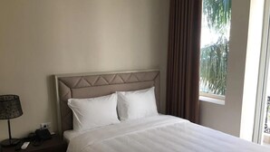 Una cama bien tendida con cabecera, una lámpara de noche y un teléfono en la mesita.