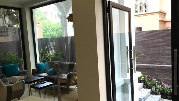 Un interior moderno con un divisor de vidrio corredizo que da a un patio. Hay una zona de estar con una mesa y sillas, y un ventilador sobre la mesa.