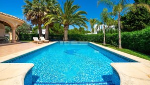 Ein Swimmingpool mit klarem, blauem Wasser, umgeben von Palmen und einer gefliesten Liegefläche.