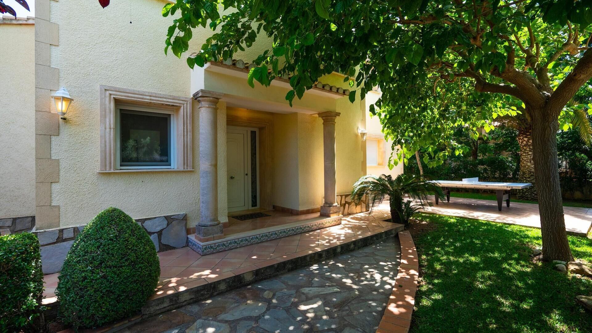Un edificio con un camino de piedra que lleva a una puerta, rodeado de vegetación y una mesa.