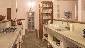 A narrow kitchen with a stone floor, a gas stove, a wooden cabinet with glass doors, and a sink. - Marula House 3BD, Diani Beach (Diani Beach)