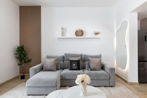 Ein modernes Wohnzimmer mit einem grauen Ecksofa, einem weißen Couchtisch und einer Topfpflanze.