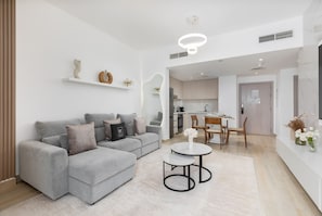Ein modernes Wohnzimmer mit einem grauen Ecksofa, einem runden Couchtisch und einem Essbereich mit einem Holztisch und Stühlen.