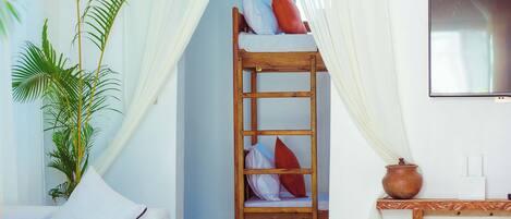 Une pièce avec un canapé blanc, une table en bois surmontée d’un vase, une suspension en rotin, une échelle en bois et un téléviseur fixé au mur.