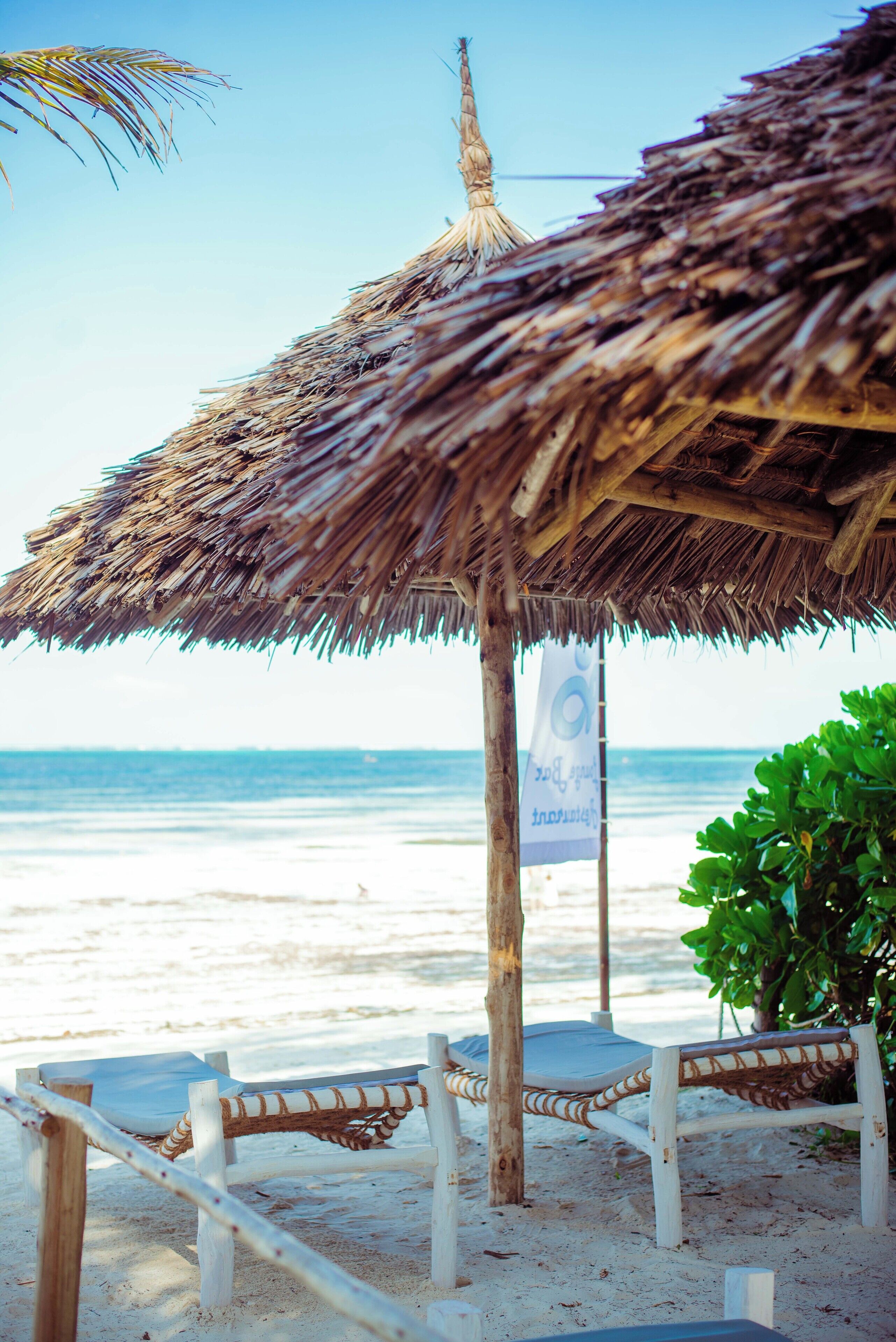 Une scène de plage avec un parasol en chaume, des chaises longues en bois et une banderole.