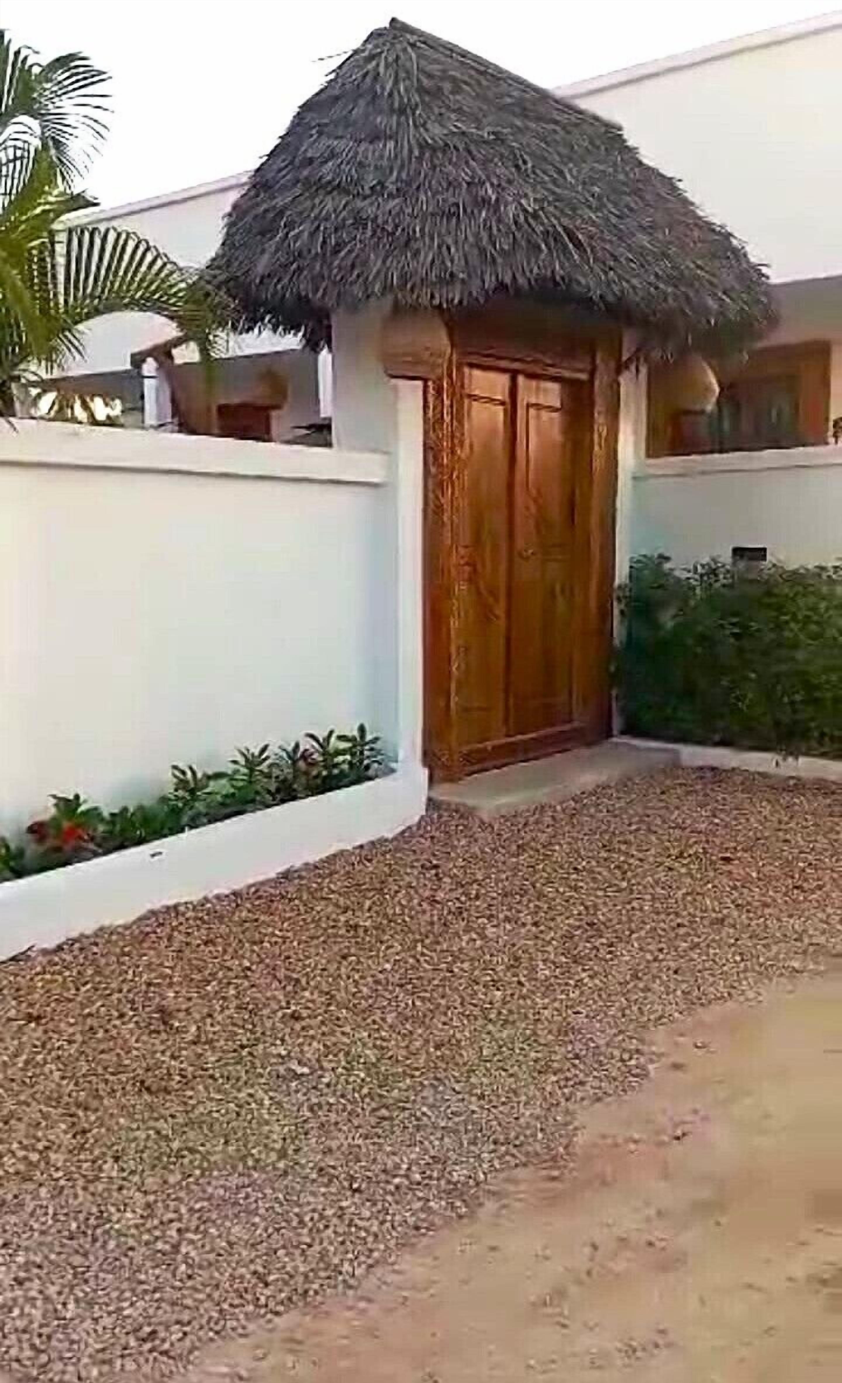 Un edificio con tetto di paglia, pareti bianche e un vialetto sterrato che conduce all'ingresso.